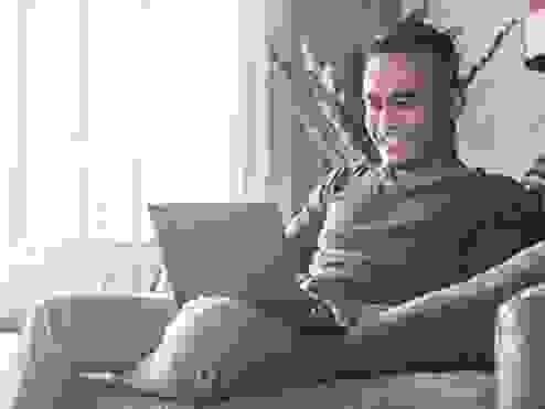 A guy sitting on his couch on a laptop smiling